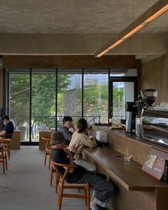 people sitting at tables in a restaurant with large windows looking out on the trees outside