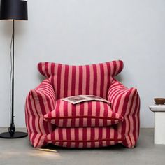 a red and white striped chair sitting next to a black lamp on a gray floor