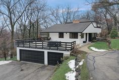 a white house with black garage doors on the front and side of it, surrounded by trees