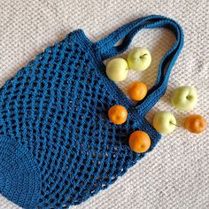 a crocheted blue bag with apples and oranges on the side sitting on a white surface