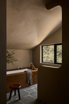 a bathroom with a bathtub and stool next to a window that looks out onto the woods