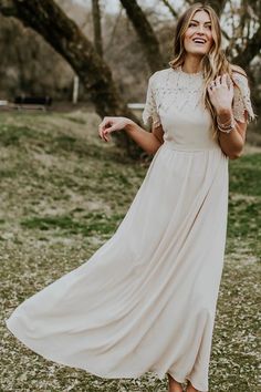 a woman in a white dress is smiling and holding her hand up to the side