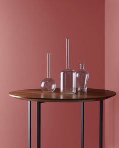 two vases on a table in front of a pink wall with black metal legs