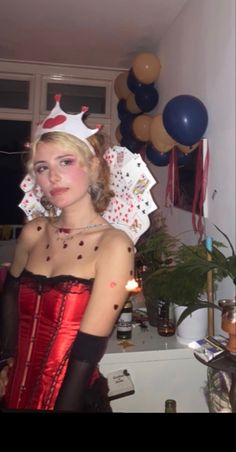 a woman in a red corset and crown standing next to a table with balloons