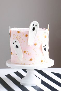 a pink cake with ghost decorations on it sitting on top of a black and white striped table