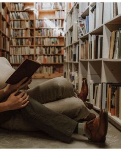 a man sitting on the floor reading a book in front of a bookshelf