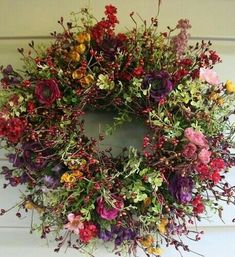 a wreath is hanging on the front door with flowers in it and greenery around it