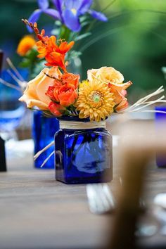 a blue vase filled with colorful flowers on top of a wooden table next to candles