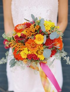 a bridal bouquet with orange, yellow and red flowers is held by a woman