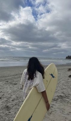 a woman holding a surfboard on top of a sandy beach next to the ocean