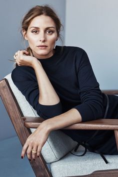 a woman sitting in a chair with her hand on her chin and looking at the camera