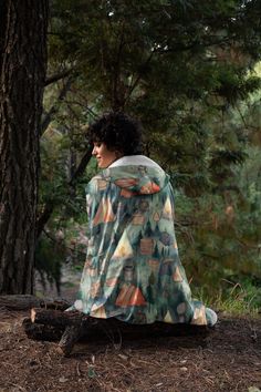 a young man sitting on top of a tree stump in the forest under a blanket