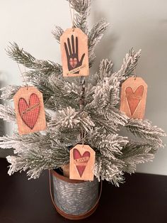 a small christmas tree with hand and heart tags hanging from it's branches in a bucket