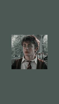 harry potter in glasses and a tie standing next to a tree with people behind him