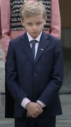 a young boy in a suit and tie standing next to a woman with her hand on her hip