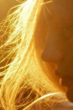 a close up of a woman's face with light shining through her hair and the sun in the background