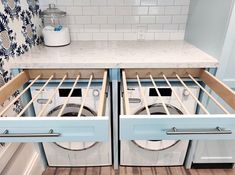 two washers are open in the middle of a kitchen with blue cabinets and white counter tops