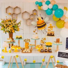 a table filled with desserts and balloons in the shape of honeybees on display