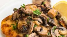 a close up of food on a plate with lemon wedges and mushrooms in the background