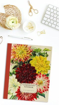 an open book sitting on top of a desk next to a keyboard and flowers in a vase