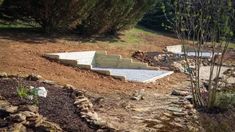 there is a concrete ramp in the middle of some dirt and rocks, with trees behind it