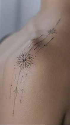 the back of a woman's shoulder with a dandelion tattoo on it