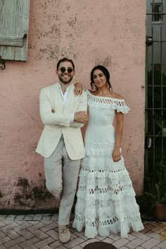 a man and woman standing next to each other in front of a pink building with shutters