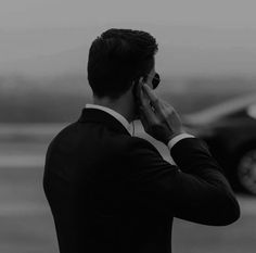 a man in a suit talking on his cell phone while standing next to a car