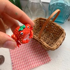 a hand holding a toy crab in front of a basket