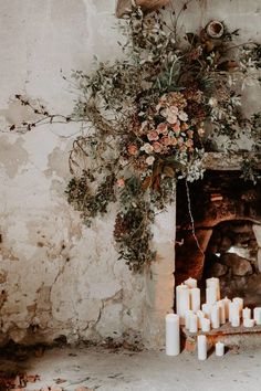 a bunch of candles sitting in front of a fire place filled with flowers and greenery