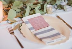 a place setting with striped napkins, silverware and greenery on the table