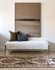 a white daybed with two pillows on it in front of a wall mounted painting