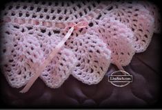 a pink crocheted baby blanket on top of a brown leather chair with a ribbon