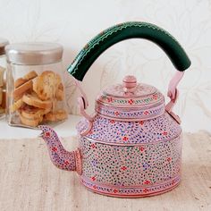 a tea pot with a green handle sitting on a table next to some crackers