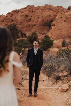 a man in a suit and tie standing on a dirt road next to a woman