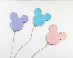 three mickey mouse head pins are shown on a white surface, one is pink and the other is blue