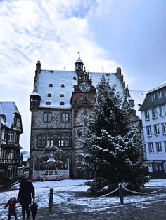 two people are walking in front of a large building with a christmas tree on it