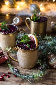 two mugs filled with cranberries and orange slices on top of a wooden table