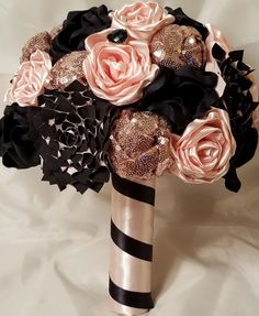 a bridal bouquet in black, pink and gold with roses on the top is sitting on a white sheet