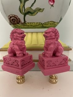 two pink foo foo statues sitting on top of a white table next to a vase