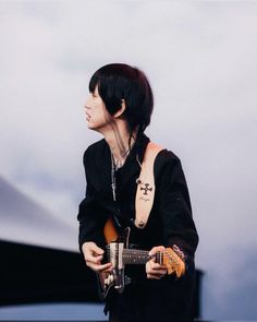 a man with black hair holding a guitar and wearing a cross tattoo on his arm