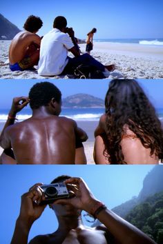 two people sitting on the beach and one is holding a cell phone in his hand