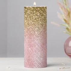 a pink and gold candle sitting on top of a table next to a vase filled with flowers