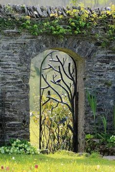 an iron gate in the middle of a stone wall with vines and flowers growing on it