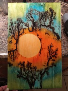 someone is holding up a painting with trees in the middle and an orange circle on it