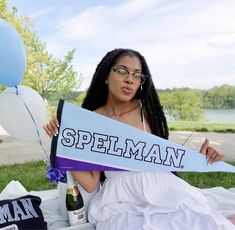 a woman sitting on the ground holding a sign that says spellman with balloons in the background