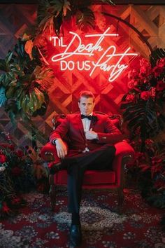 a man in a red suit sitting on a red chair next to plants and flowers