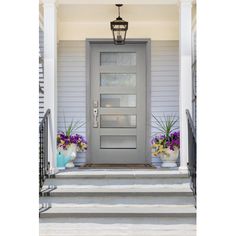 a gray front door with two flower pots on the steps and a light fixture above it