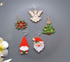 four christmas themed beaded earrings on a plate next to flowers and a white flower