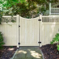 a white fence with two gates in front of some trees and bushes on the other side